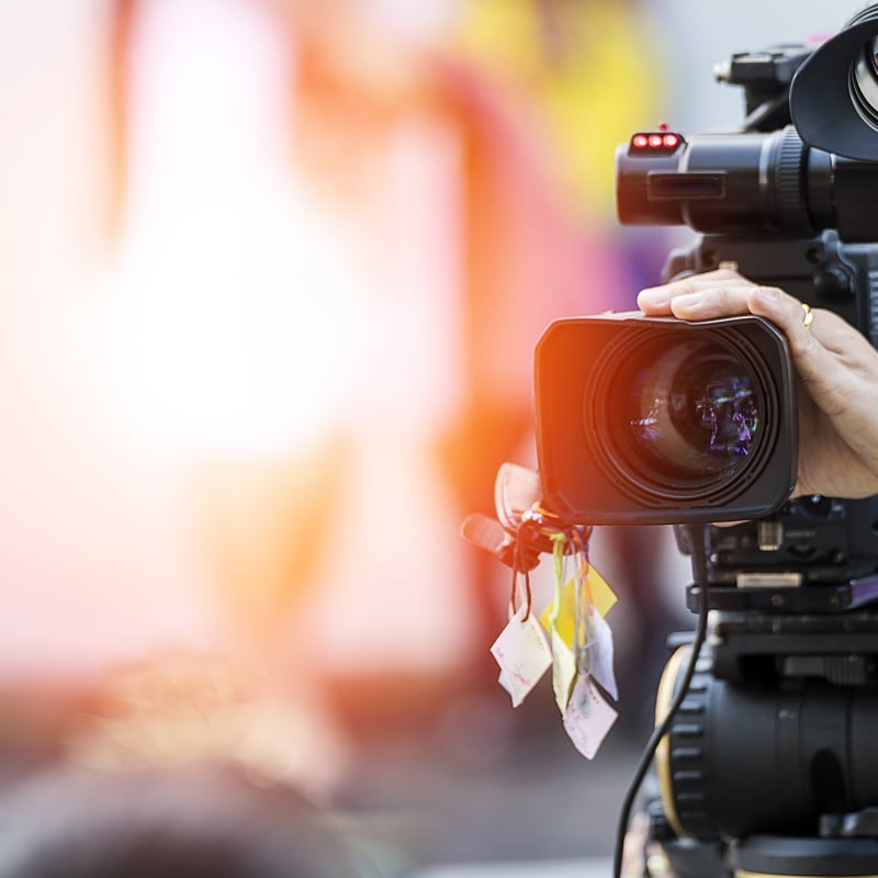 Caméra Vidéo Professionnelle en Plein Tournage d'Événement Gros plan d'une caméra vidéo professionnelle tenue par un cadreur lors d'un événement sous un éclairage vif.