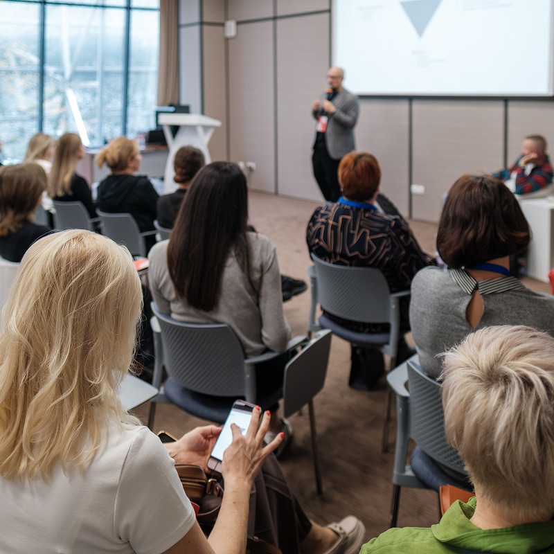 Conférence professionnelle : Présentation et public attentif Femme utilisant son smartphone lors d'une conférence professionnelle avec un présentateur et son auditoire.