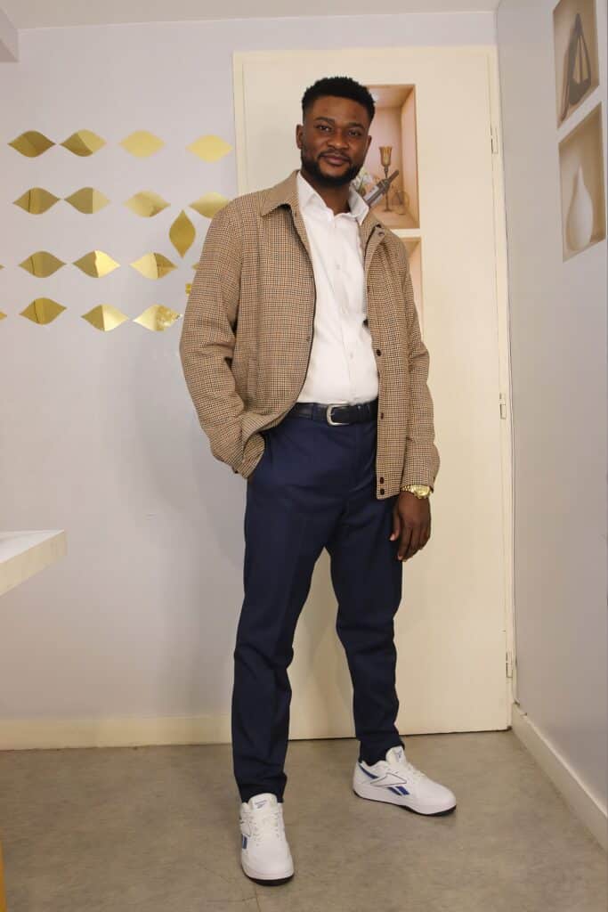 Style Homme : Look Chic avec Veste à Carreaux Beige Homme en veste à carreaux beige, pantalon bleu marine et baskets blanches Reebok posant avec assurance.